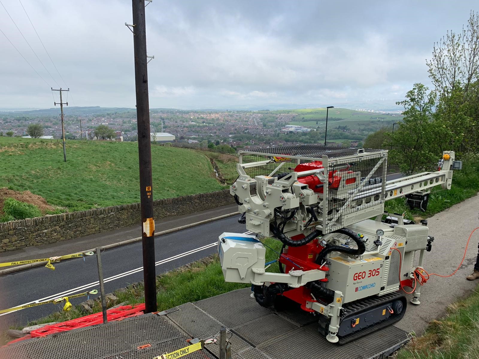 Geotron Comacchio GEO305 tracked rotary rig on a hillside road above a town