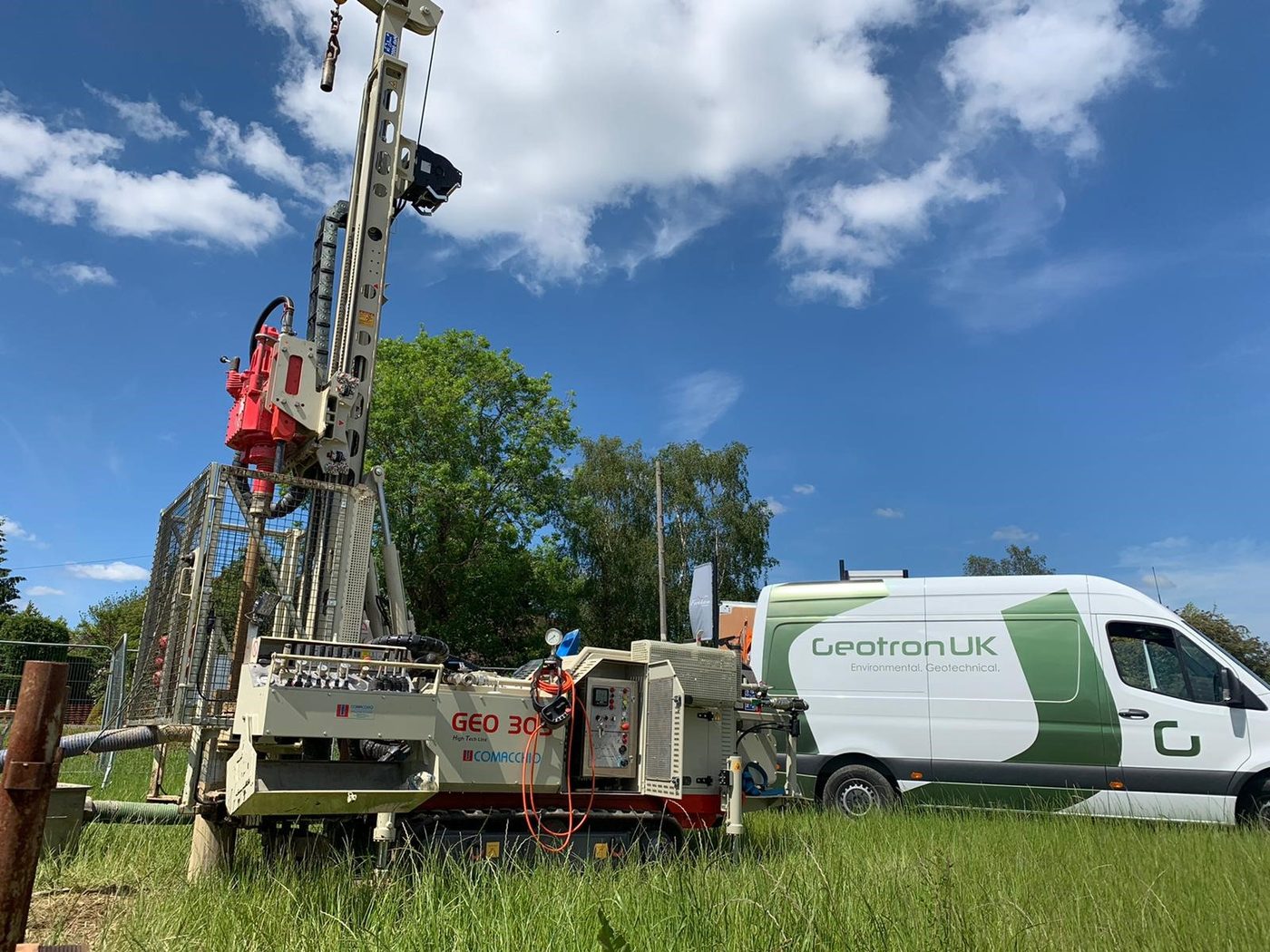 Geotron Comacchio GEO305 rotary rig mast up in a green field beside the company van